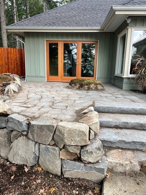 Custom stone patio and fencing — flagstone terrace with cedar doors and stone retaining wall